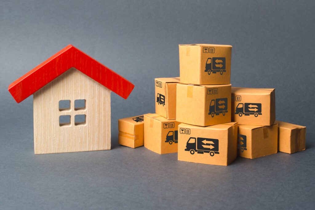 Piles of boxes beside a wooden house figurine in the concept of 'What Factors Influence the Cost of a Man and Van Service in Chelsea'.