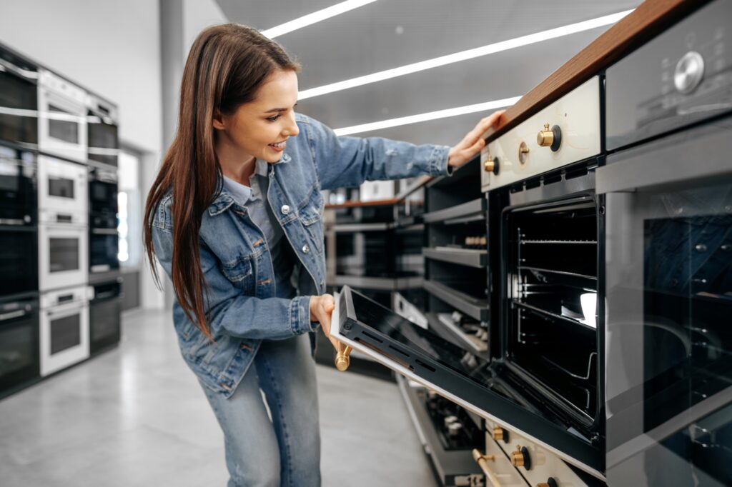 A young woman inspecting an electric stove in a store to be delivered by a Man and Van