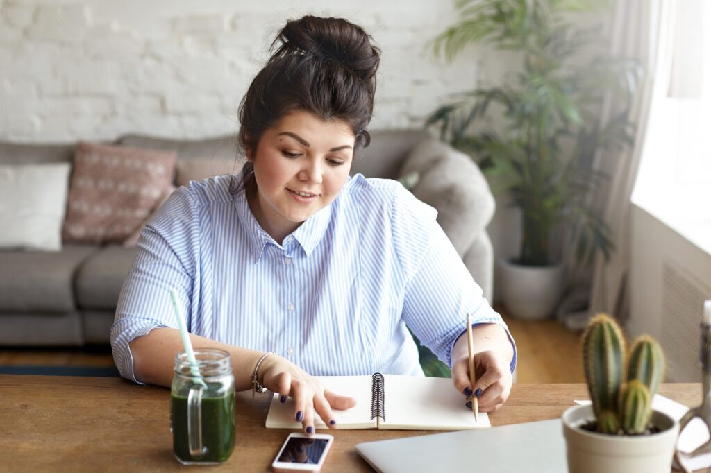 A woman holding a pen with a notebook, mobile phone, and laptop in the concept of 'How to Get a Quote for a Man and Van Service'.